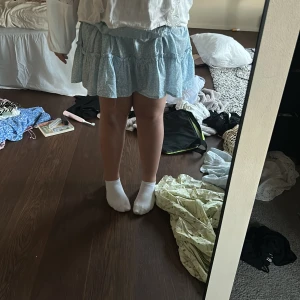 Ljusblå volangkjol med småmönster - Säljer en ljusblå kortkjol med volanger och vitt småmönster. Kjolen har en luftig och söt design med flera lager och resår i midjan. Perfekt för dig som gillar en feminin och somrig stil.