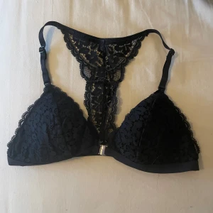 Svart spets bralette - Säljer en svart bralette med fina spetsdetaljer och broderat mönster i ryggen. Axelbanden är justerbara och modellen har en dekorativ rygg. Perfekt för att ge outfiten en extra touch.