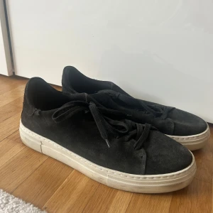 Svarta mockasneakers från Selected Homme - Säljer ett par svarta sneakers från Selected Homme i mocka med vita, platta sulor. Skorna har rund tå och klassisk snörning. Perfekta för dig som gillar stilrena och enkla skor med en modern touch.
