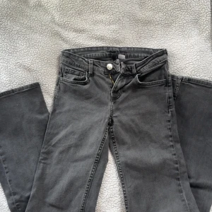 Grå jeans med bootcut - Säljer ett par grå jeans med bootcut-modell och klassisk femficksdesign. Byxorna har dragkedja och knapp framtill samt raka bakfickor. Perfekta för dig som gillar en tidlös look.