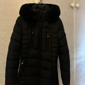 Svart dunjacka med pälskant från Wellensteyn - Säljer en svart dunjacka från Wellensteyn med pälskantad huva och flera dragkedjefickor. Jackan har quiltad design och hög krage som skyddar mot kyla. Perfekt för kalla dagar och snygg till många outfits. (ordinarie pris 4 980 kronor)