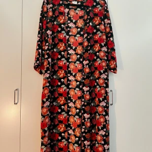 Blommig lång kimono med vida ärmar - Säljer en svart lång kimono från Zalando, i märket JDY, med stora blommor i rött, orange och vitt. Den har vida, långa ärmar som är 3/4 långa (kommer ej hela vägen ner till handleden) och ett rakt fall. På tredje bilden ser man att den har slits vid sidorna längst ner på kimonon. Perfekt för dig som gillar färgstarka mönster och vill sticka ut. Har används 2-3ggr. Storleken är 40. Priset kan diskuteras. 