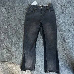 Svarta jeansbyxor från Gallery Dept. - Säljer ett par svarta jeansbyxor från Gallery Dept. med raka ben och unika svarta paneler längs sidorna. Byxorna har klassisk femficksdesign, gylf med dragkedja och knapp samt råa kanter nertill.