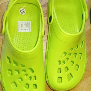 Neongula sandaler med hålmönster - Säljer ett par neongula sandaler med hålmönster och justerbar hälrem. Skorna är tillverkade i syntetmaterial och har en platt sula. Perfekta för sommaren och strandhäng!