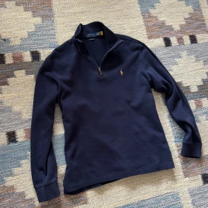 Mörkblå quarter-zip tröja från Polo Ralph Lauren - Säljer en klassisk mörkblå quarter-zip tröja från Polo Ralph Lauren med liten broderad logga på bröstet. Tröjan har lång ärm, hög krage och dragkedja vid halsen. Perfekt för en stilren och avslappnad look. Skick 9.5/10