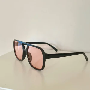 Svarta solglasögon med rosa glas - Snygga solglasögon med svart båge och rektangulär form🤵🏼Glasen är ljusrosa och ger en cool retrovibe. Perfekt accessoar för att lyfta din stil😎