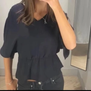 Svart blus med v-ringning - Säljer en svart blus med v-ringning och trekvartsärmar. Blusen har en lätt markerad midja och en lös passform upptill. Perfekt att styla med jeans eller kjol. Snören vid ärmen 