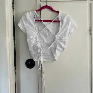 Vit T-shirt med öppen rygg och snörning - Säljer en vit T-shirt med öppen rygg och snörning. Perfekt till sommaren och enkel att matcha med ex. jeans eller kjol. Superfin och trendig🥰använd ett par gånger.