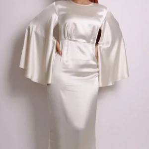 Maxi studentklänning i satin med vida ärmar - Elegant vit långklänning i glansigt satinmaterial med rund halsringning och dramatiskt vida, långa ärmar.  Köpte den för 3 åren sen för min student och har använt den bara en gång! Köpte den för 1500! 