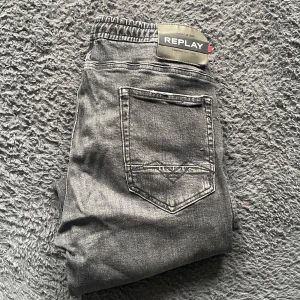 Replay jeans  - Säljer ett par grå jeansbyxor från Replay med slitna detaljer och elastisk midja. Byxorna har klassisk femficksdesign och smal passform. Perfekta för dig som gillar en modern och avslappnad stil. Jeansen har snören som går att ta bort om man vill det.