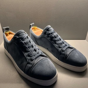 Blåa mockasneakers från Christian Louboutin - Säljer ett par stilrena blåa sneakers i mocka från Christian Louboutin med klassisk röd sula. Skorna har rund tå, snörning och vit platt sula. Perfekta för dig som vill ha en lyxig och clean look.