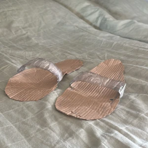 Handgjorda sandaler av kartong  - Unika sandaler tillverkade av kartong med breda remmar av tejp. Ovansidan är dekorerad med röda kritstreck och siffror. Perfekt för dig som vill ha något annorlunda och kreativt på fötterna.