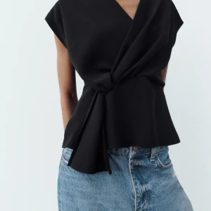 Svart omlottopp från Zara - Säljer en svart omlottopp från Zara med knutdetalj framtill. Aldrig använd, endast testad. Storlek XL, liten i storleken så passar även storlek L/M beroende på hur man vill att den ska sitta och hur lång man är❣️