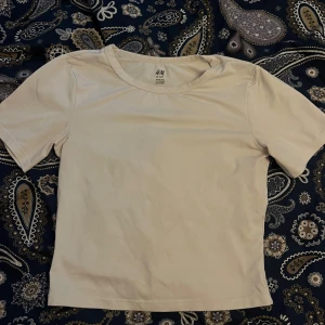 Beige sporttopp från H&M 🤍 - En enkel och stilren beige sporttopp från H&M med rund halsringning och korta ärmar. Perfekt för träning eller en avslappnad look. Tillverkad i mjukt och stretchigt material för extra komfort.