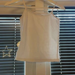 Vit linnetopp med smala axelband - Säljer en enkel och stilren vit linnetopp med smala axelband. Perfekt att matcha med jeans eller kjol för en clean look. Toppen har en rak passform och ärmlös design.