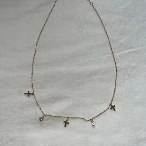 Guldfärgat halsband med kors och stenar - Säljer ett tunt guldfärgat halsband med tre små kors och två gnistrande stenar som hängen. Kedjan är fin och diskret, perfekt för att ge en extra touch till din stil. Guldplatterat, köpare stär för frakt, pris kan diskuteras.