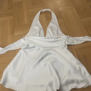 Vit omlottklänning i satin med djup v-ringning - Supersnygg vit omlottklänning från ZARA i glansigt satinmaterial. Klänningen har djup v-ringning, knytband i midjan och är ärmlös. Endast provad och har prislappen kvar. Bild på kan skickas privat :) 