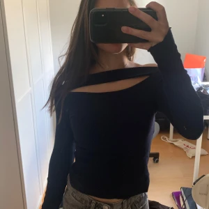 Mörkblå offshoulder topp med cut-out - Säljer en mörkblå långärmad topp med unik offshoulder-design och cut-out detalj vid halsen. Snygg och trendig modell som passar perfekt till jeans eller kjol. Materialet känns mjukt och stretchigt.