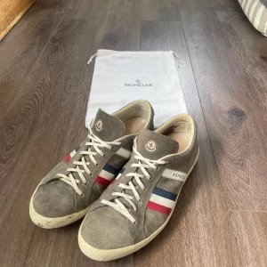 Grå/bruna sneakers från Moncler - Säljer ett par gråa/bruna sneakers från Moncler. Ganska sällsynt och eftertrakad modell, storlek 43 men italiensk storlek så lite större skulle jag säga. Inga defekter utöver att lädret har släppt lite i hälen på vänster sko, inget som hindrar funktion eller syns. Lite smutsiga såklart men inga defekter utöver de. Dustbag medföljer tyvärr inget kvitto. Äkta såklart