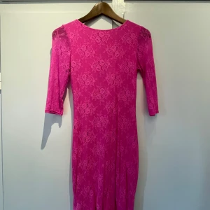 Rosa spetsklänning med dragkedja - Säljer en rosa klänning med blommig spets och trekvartsärm. Klänningen har en lång dragkedja bak och är figurnära i modellen. Perfekt för dig som vill sticka ut med färg och detaljer!