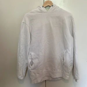 Vit hoodie från SMOG - Säljer en enkel och stilren vit hoodie från SMOG i storlek L. Tröjan har huva, magficka och är tillverkad i mjukt material. Perfekt för en avslappnad look och passar till det mesta.