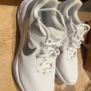 Vita Nike sneakers med silvrig swoosh - Säljer ett par helt nya vita Nike running sneakers med silvrig swoosh på sidan. Endast provade en gång inomhus. För små för mig så säljer vidare. 