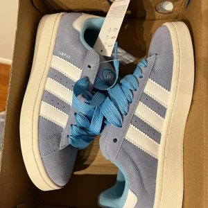 Ljusblå Adidas Campus sneakers - Säljer ett par fräscha Adidas Campus sneakers i ljusblå mocka med vita ränder och vit sula. Skorna har blå skosnören och en mjuk blå insida. Perfekta för dig som gillar klassisk streetstil med en twist. Aldrig använda storlek 38