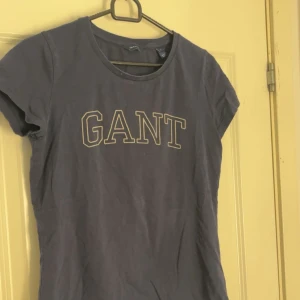 Mörkblå t-shirt från GANT - Säljer en mörkblå t-shirt från GANT med klassisk logga tryckt framtill. T-shirten har rund halsringning och korta ärmar. Perfekt för en avslappnad och stilren look. 