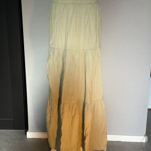 Beige långkjol med volang - En beige långkjol med volangdetaljer och resår i midjan. Kjolen har en luftig och avslappnad passform.