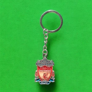Liverpool FC nyckelring i metall - Snygg nyckelring med Liverpool FC:s klassiska klubbmärke i silver och rött. Perfekt accessoar för alla fotbollsfans som vill visa sitt stöd för laget. Metallkedja och ring för enkel fastsättning på nycklar eller väska.