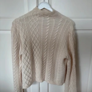 Beige stickad tröja från & Other Stories - Säljer en beige stickad tröja från & Other Stories med kabelstickat mönster och rund hals. Tröjan har lång ärm och är perfekt för lager-på-lager under kyligare dagar. Klassisk och stilren design.