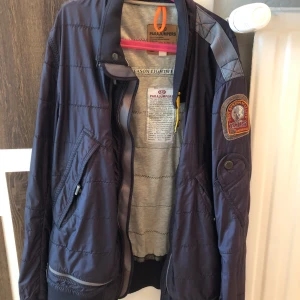 Blå lättviktsjacka från Parajumpers  - Säljer en blå lättviktsjacka från Parajumpers med broderad patch på ärmen och dragkedja framtill. Jackan har hög krage och flera praktiska fickor. Perfekt för dig som vill ha en snygg och funktionell jacka till vardags. STORLEK M.