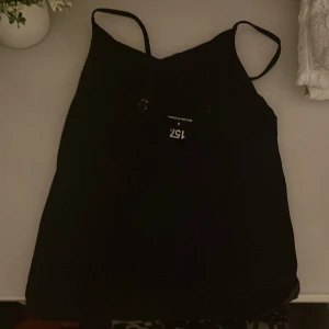 Svart linnetopp från 157 - En enkel och stilren svart linnetopp från 157 med smala axelband. Perfekt att matcha med jeans eller kjol för en clean look. Gjord i mjukt material som känns skönt mot huden.