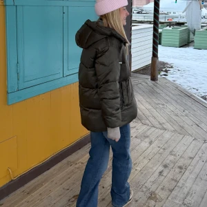 Mörkgrön pufferjacka med huva - Säljer en mörkgrön pufferjacka med huva och dragkedja framtill. Jackan är vadderad och har en oversized passform som ger en cool och avslappnad look. Perfekt för kalla dagar och enkel att styla med jeans eller mjukisbyxor.