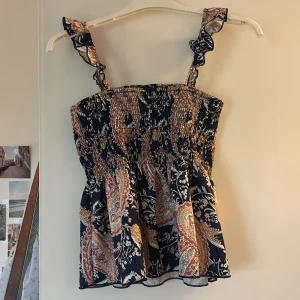 Super fin smockad sommartopp - Säljer en blus med smockdetaljer och ett färgglatt mönster i blått, rött och gult. Blusen har breda axelband och en luftig passform, perfekt för sommardagar 🤍