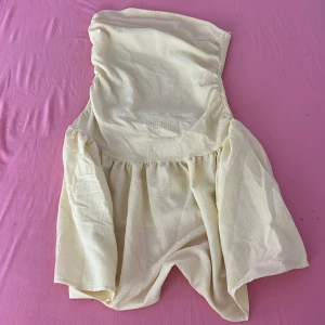 Gul axelbandslös kortklänning - Superfin ljus kortklänning i axelbandslös modell med smockad rygg och volangig kjol. Köpt utomlands!!