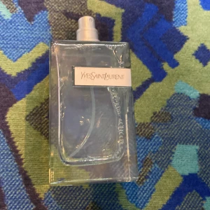 Yves Saint Laurent parfym - Stilren parfym från Yves Saint Laurent i en rektangulär, transparent glasflaska med vit etikett och svart text. Flaskan har en enkel sprayfunktion och innehållet är ljusblått. Perfekt för dig som gillar klassisk och elegant design. Ingen box ingen kvitto, inget lock nästan helt ny, ny pris runt 1699, mitt pris 899, pris Kl diskuteras vid snabb köp