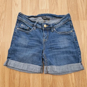 Blå jeansshorts med uppvik - Klassiska blå lågmidjade midlånga jeansshorts från ESMARA med fem fickor, bälteshällor och snygga uppvikta benslut. Perfekta för sommaren och lätta att matcha med allt. Gjorda i slitstarkt denimtyg med knapp och dragkedja framtill.
