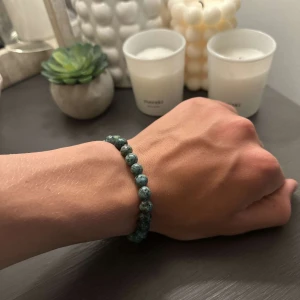 Grönt pärlarmband med stenmönster - Snyggt armband med runda pärlor i olika nyanser av grönt och blått, med ett naturligt stenmönster. Pärlorna är trädda på elastisk tråd vilket gör det enkelt att ta på och av. Perfekt accessoar för att ge din outfit en cool touch.
