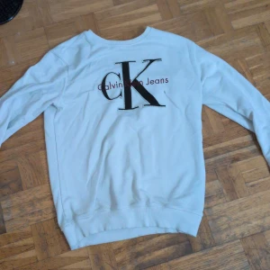 Vit sweatshirt från Calvin Klein Jeans - Vit sweatshirt från Calvin Klein Jeans med stor broderad CK-logga och text på bröstet. Tröjan har rund halsringning, långa ärmar och är gjord i mjuk bomull. Perfekt för en clean och stilren look.