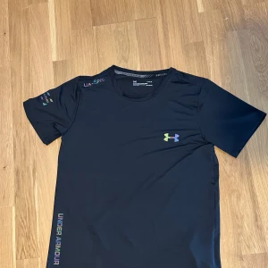 Svart Under Armour HeatGear t-shirt - Svart t-shirt från Under Armour med färgglad logga på bröstet och tryck på ärmen och sidan. Tillverkad i funktionsmaterial HeatGear som andas och passar perfekt för träning. Klassisk rund hals och korta ärmar för en sportig look.