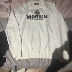 Morris tröja - Vit stickad tröja från Morris med rund halsringning och ribbade muddar. Stor broderad Morris-logga och brittisk flagga framtill ger en klassisk och sportig vibe. Perfekt för dig som gillar stilrena och tidlösa plagg med snygga detaljer. Tröjan är i storlek M men kan även passa S, DM för fler frågor!