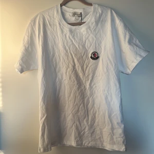 Vit Moncler t-shirt - Vit t-shirt från Moncler i bomull med klassisk rund hals och korta ärmar. På bröstet sitter en broderad Moncler-logga. otroligt snygg till sommaren och tag finns kvar! Pris kan diskuteras!