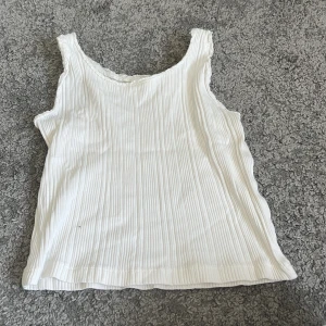 Vit ribbad linnetopp från Zara - Supersöt vit ribbad linnetopp från Zara med spetskant runt halsringningen. Perfekt för varma dagar och enkel att matcha med jeans eller kjol. Toppens material känns mjukt och luftigt, och den är ärmlös för en chill vibe.