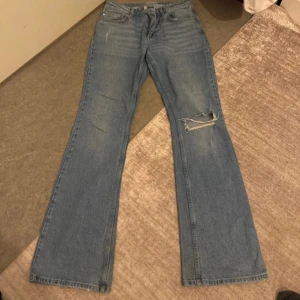 Blå bootcut jeans från Gina Tricot - Snygga ljusblå bootcut jeans från Gina Tricot, modell Perfect Jeans. Klassisk femficksdesign, slitning och hål på ena knät samt råare kant nertill. Jeansen har en rak, lite utsvängd passform och är gjorda i klassiskt denimtyg.