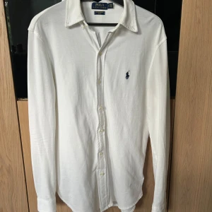 Vit skjorta från Polo Ralph Lauren - Klassisk vit skjorta från Polo Ralph Lauren i featherweight mesh. Skjortan har lång ärm, knappar framtill och den ikoniska broderade loggan på bröstet. Perfekt passform och lätt material som känns fräscht hela dagen.