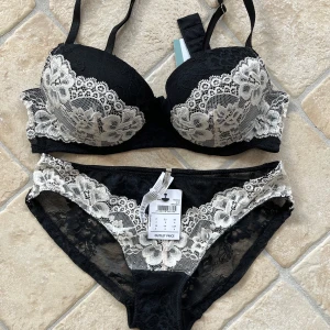 Svart set BH + trosa från Intimissimi - Fin svart BH med tillhörande trosa från Intimissimi med kontrasterande vit spets och blommiga detaljer. Axelbanden är justerbara och kuporna är vadderade för extra form. Storlek trosa: S