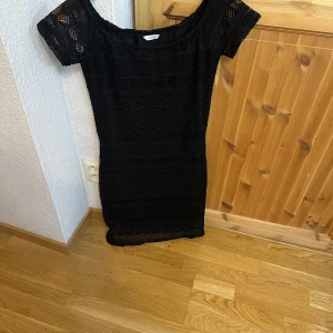 Svart spetsklänning med kort ärm - Supersnygg svart kortklänning med genombruten spets och coola mönsterdetaljer. Klänningen har korta ärmar och en figurnära passform som framhäver siluetten. Perfekt för dig som vill sticka ut med en elegant men edgy look.