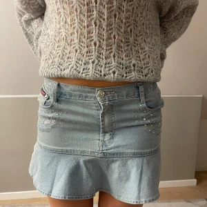 Ljusblå jeanskjol med volang och pärlor - Supersöt ljusblå jeanskjol från YUKEJEANS med volangkant nertill och snygga pärldetaljer både fram och bak. Klassisk femficksmodell med knapp och dragkedja. Perfekt för dig som gillar denim med lite extra bling.