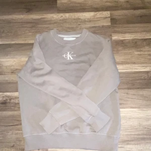 Beige Calvin Klein Jeans sweatshirt - Snygg beige sweatshirt från Calvin Klein Jeans med broderad logga på bröstet. Tröjan har rund halsringning, långa ärmar och är gjord i mjuk bomullsmix. Perfekt för en chill och stilren look.